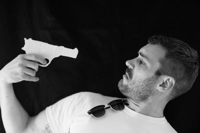 Shirtless man attempting suicide with gun against black background