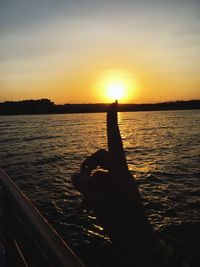 Silhouette man hand by sea against sky during sunset