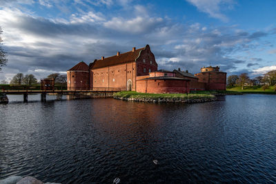 Buildings by river against cloudy sky