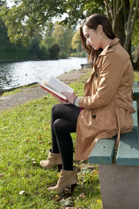 Side view of woman reading book while sitting on bench