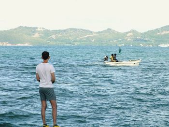 Rear view of men standing on sea against mountains