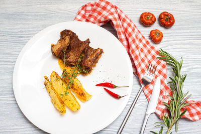 Fried lamb ribs with baked potatoes slices. thyme herbs. one portion on a big white plate.