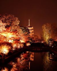 Illuminated city by river against sky at night