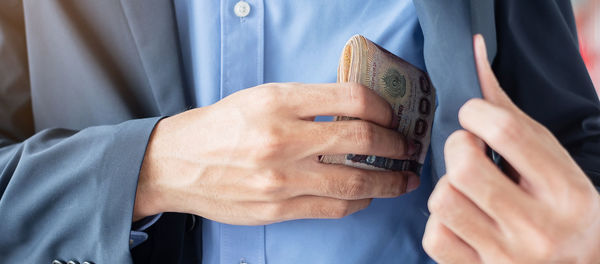 Midsection of businessman keeping paper currency in pocket