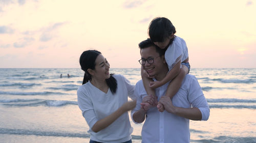 Friends standing on beach against sky during sunset