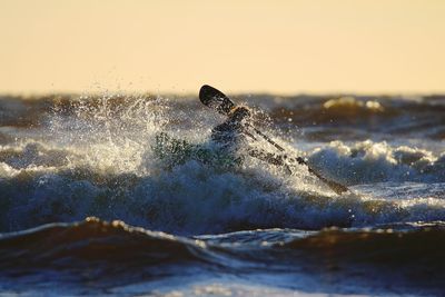 Silhouette person kayaking in sea against clear sky during sunset