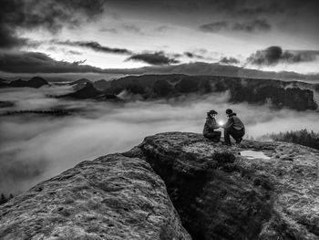 Rear view of man sitting on rock against sky