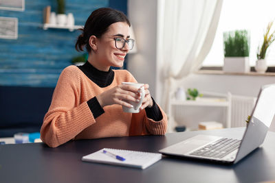 Young woman using phone while sitting on table