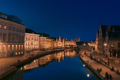 Illuminated buildings by river against sky at night