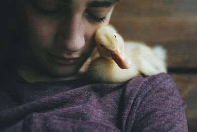 Close-up of teenage boy with duckling sitting at home