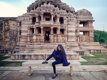 Full length of woman sitting on bench against historic building