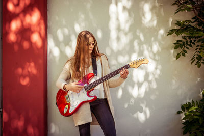 Beautiful girl playing guitar while standing by wall