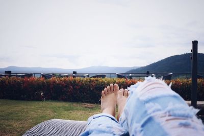 Low section of woman relaxing on chair at field against sky