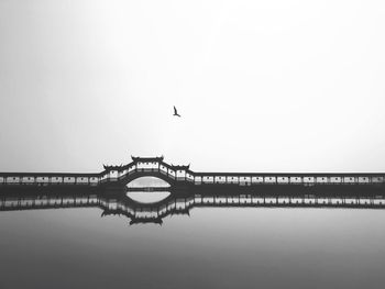 Silhouette birds on bridge over lake against sky