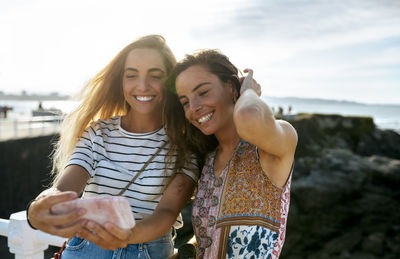 Smiling young sisters taking selfie at beach during weekend