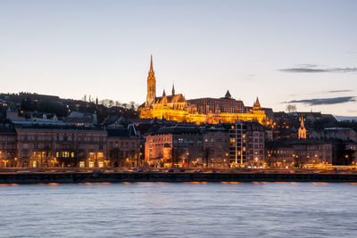 Illuminated buildings by danube river against sky at dusk