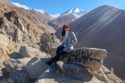 Full length of woman sitting on rock against mountains