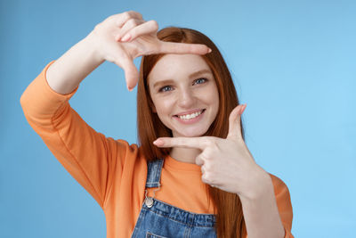 Portrait of smiling young woman making finger frame against blue background
