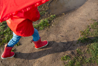 Child plays with umbrella after the rain in red rubber boots and a raincoat.