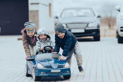 Three happy children playing with big old toy car in countryside, outdoors.