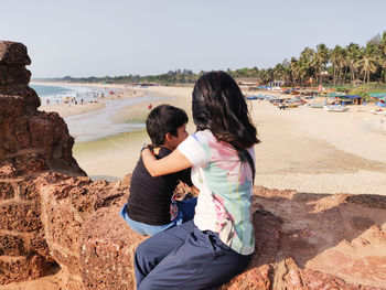 Rear view of family enjoying at beach against sky