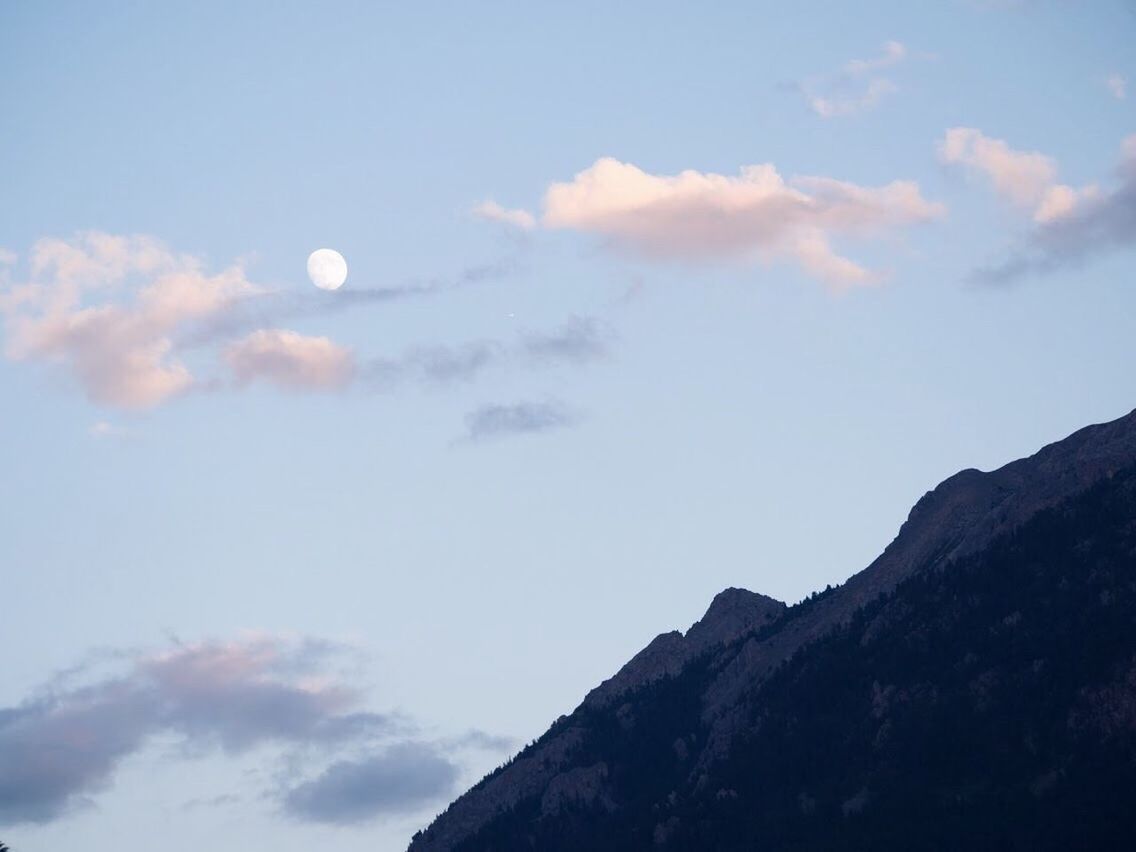 LOW ANGLE VIEW OF MOON IN MOUNTAINS AGAINST SKY