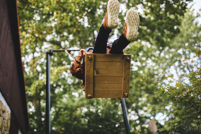 Low angle view of boy sitting on swing against trees