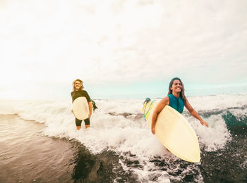 Friends carrying surfboards while walking in sea