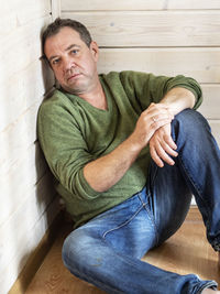 Portrait of depressed mature man sitting on hardwood floor at home
