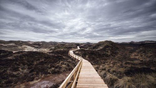 Boardwalk on dramatic landscape against cloudy sky