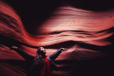 Woman with arms outstretched standing against rock 