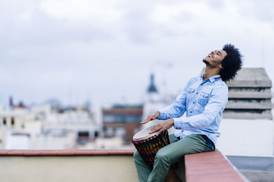 Young woman looking away while sitting against sky