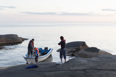 Family standing with motorboat in baltic sea against sky during sunset