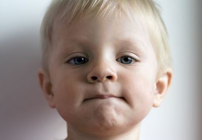 Close-up portrait of cute boy biting lips against white wall