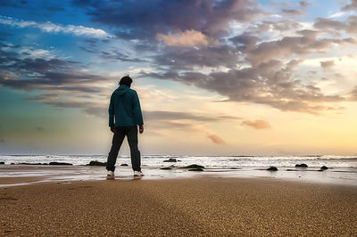 Rear view of man standing on beach during sunset