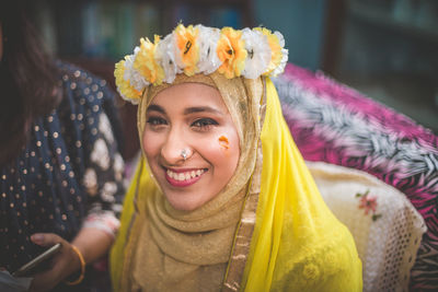 Portrait of smiling young woman in traditional clothing and flowers at home