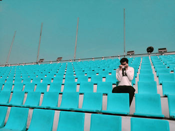 An unknown person sitting on blue seat at stadium 