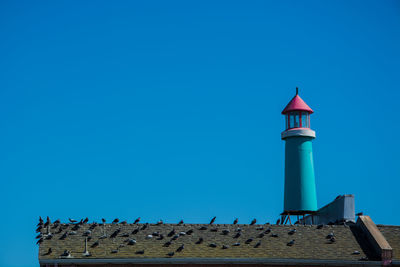 Low angle view of lighthouse against building against clear blue sky