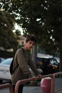 Portrait of teenage boy holding railing while standing outdoors