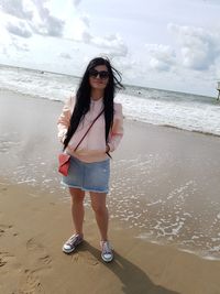 Beautiful woman standing on shore at beach against sky