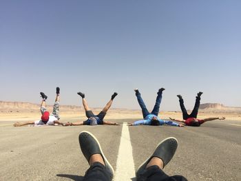 Men with legs in air lying on road against sky
