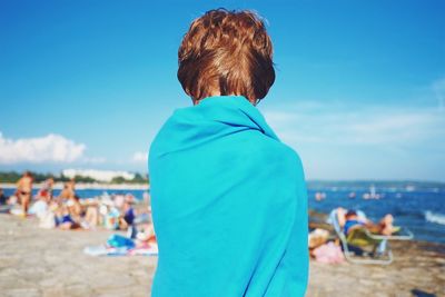 Rear view of boy standing at beach against blue sky