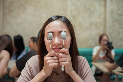 Young woman holding spoons while sitting at restaurant