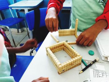 Midsection of people creating art product with toy blocks on table 