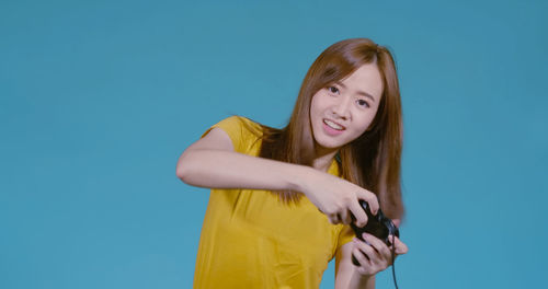 Portrait of young woman standing against blue background