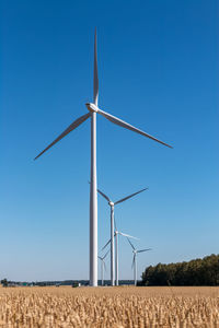 Windmills on scenic agricultural field against clear blue sky