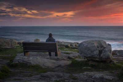 Man watching a stunning sunset sitting on a bench on the coast