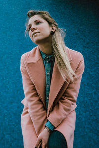 Young woman looking away while standing against blue wall