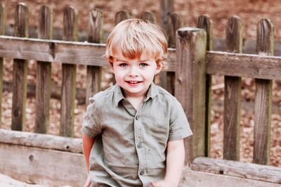 Portrait of smiling boy sitting on bench by fence