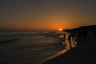 People on beach against sky during sunset